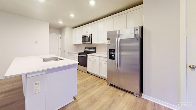 kitchen with a kitchen island, appliances with stainless steel finishes, white cabinets, and light hardwood / wood-style flooring