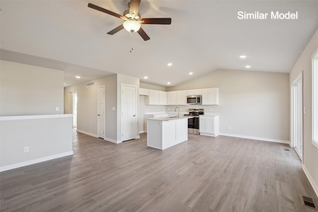 kitchen with appliances with stainless steel finishes, white cabinets, a center island with sink, vaulted ceiling, and light wood-type flooring