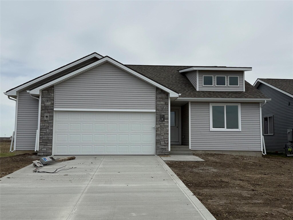 505 Fireside Dr NW, Bondurant, IA 50035 - view of front of house featuring stone siding, driveway, roof with shingles, and a garage