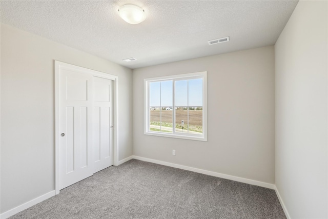 unfurnished bedroom featuring visible vents, a closet, baseboards, a textured ceiling, and carpet flooring