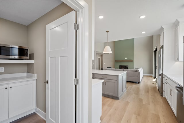 kitchen with white cabinetry, appliances with stainless steel finishes, kitchen peninsula, pendant lighting, and light hardwood / wood-style floors