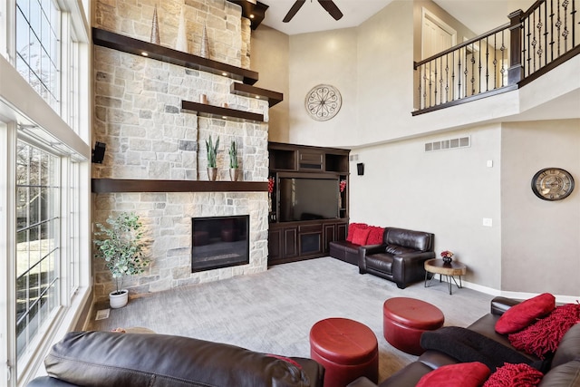 living room with a towering ceiling, a stone fireplace, ceiling fan, and carpet