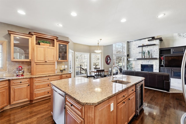 kitchen with pendant lighting, an island with sink, sink, wine cooler, and light stone counters