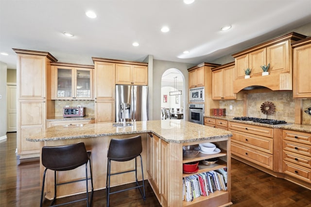 kitchen with light brown cabinets, appliances with stainless steel finishes, dark hardwood / wood-style floors, an island with sink, and light stone countertops