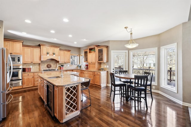 kitchen featuring sink, stainless steel appliances, light stone counters, wine cooler, and an island with sink