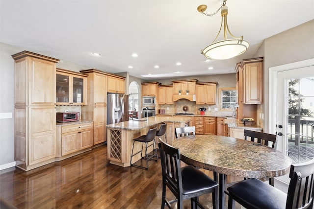 kitchen featuring appliances with stainless steel finishes, backsplash, a center island, light stone counters, and decorative light fixtures