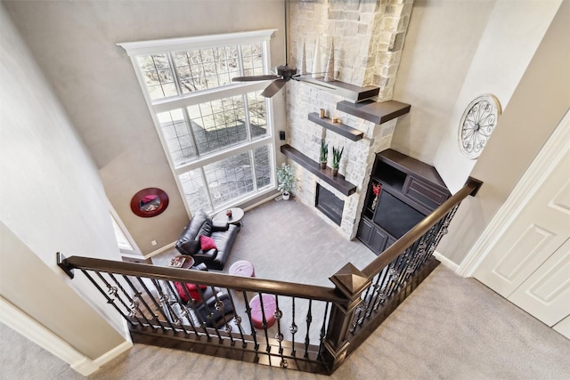 stairs featuring a towering ceiling, a fireplace, ceiling fan, and carpet flooring