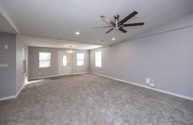 unfurnished living room featuring ceiling fan with notable chandelier, a textured ceiling, and carpet