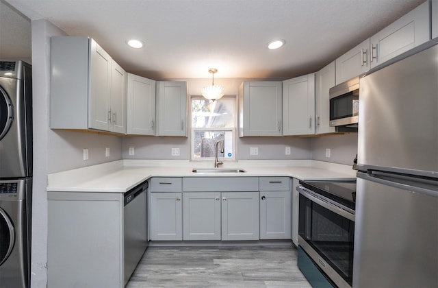 kitchen featuring stacked washer and clothes dryer, sink, decorative light fixtures, appliances with stainless steel finishes, and light hardwood / wood-style floors