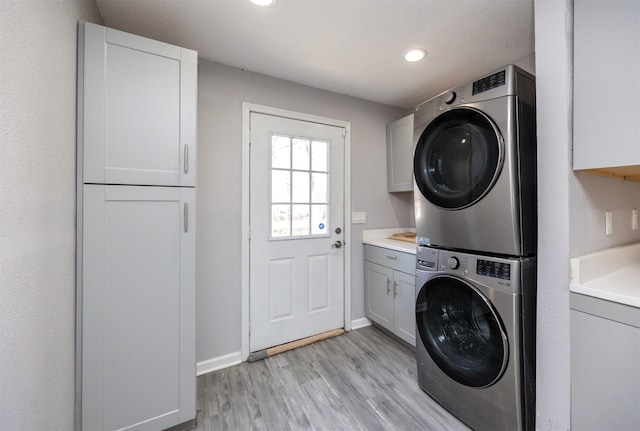 washroom featuring cabinets, stacked washer and dryer, and light hardwood / wood-style flooring