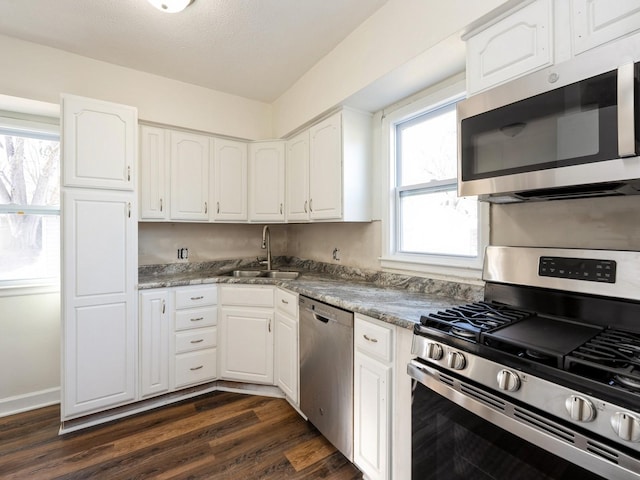 kitchen featuring sink, appliances with stainless steel finishes, dark stone countertops, dark hardwood / wood-style floors, and white cabinets