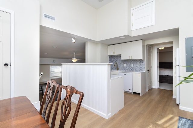 kitchen with tasteful backsplash, white cabinetry, white dishwasher, and light hardwood / wood-style flooring