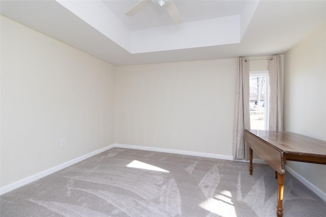 carpeted spare room featuring a tray ceiling and ceiling fan