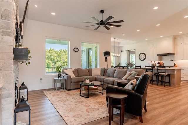 living room featuring ceiling fan, a healthy amount of sunlight, a stone fireplace, and light hardwood / wood-style flooring