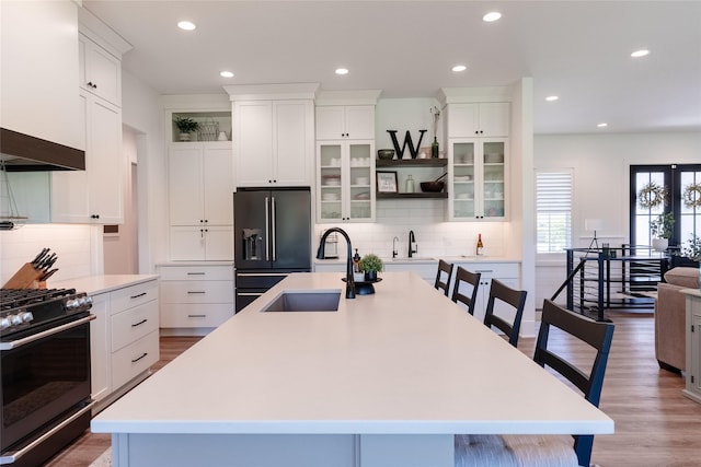 kitchen featuring high end black refrigerator, range with gas cooktop, an island with sink, white cabinets, and a kitchen bar