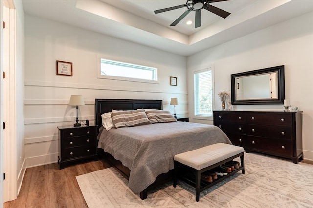 bedroom with light hardwood / wood-style flooring, a raised ceiling, and ceiling fan