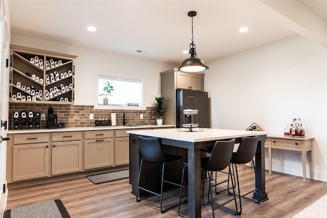 kitchen featuring light hardwood / wood-style flooring, hanging light fixtures, backsplash, a center island, and black fridge