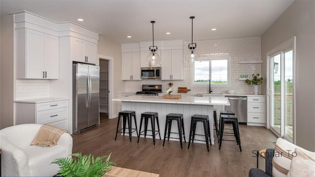 kitchen featuring appliances with stainless steel finishes, white cabinetry, hanging light fixtures, dark hardwood / wood-style floors, and a center island