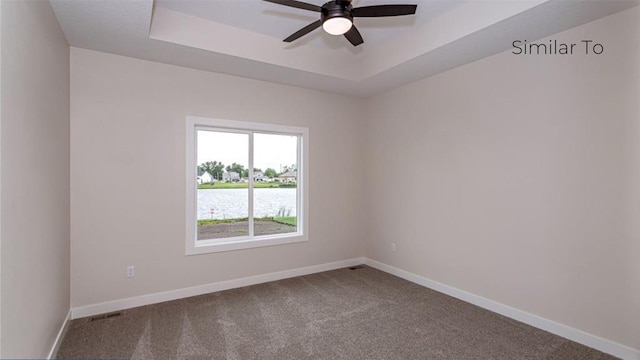 empty room with carpet flooring, a raised ceiling, ceiling fan, and a water view