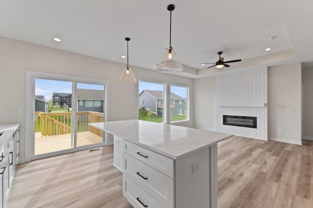 575 NW Prairie Rose Ln, Waukee, IA 50263 - kitchen featuring light wood-type flooring, a tray ceiling, a kitchen island, ceiling fan, and white cabinetry