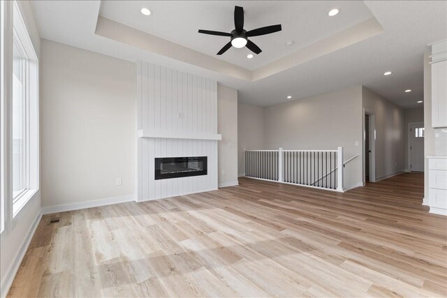 575 NW Prairie Rose Ln, Waukee, IA 50263 - unfurnished living room featuring a raised ceiling, light wood-type flooring, ceiling fan, plenty of natural light, and recessed lighting