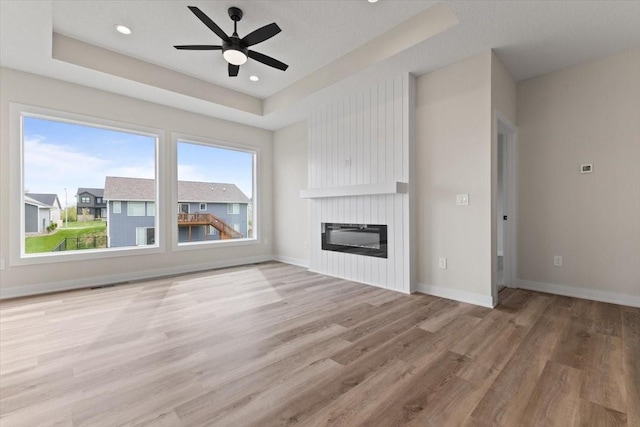 575 NW Prairie Rose Ln, Waukee, IA 50263 - unfurnished living room featuring wood finished floors, ceiling fan, a raised ceiling, a fireplace, and baseboards