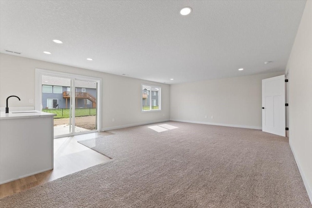 575 NW Prairie Rose Ln, Waukee, IA 50263 - unfurnished living room with a sink, healthy amount of natural light, light colored carpet, baseboards, and recessed lighting