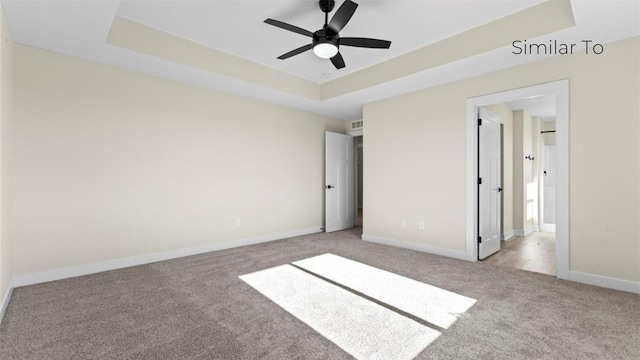 unfurnished bedroom with ceiling fan, a tray ceiling, and light carpet