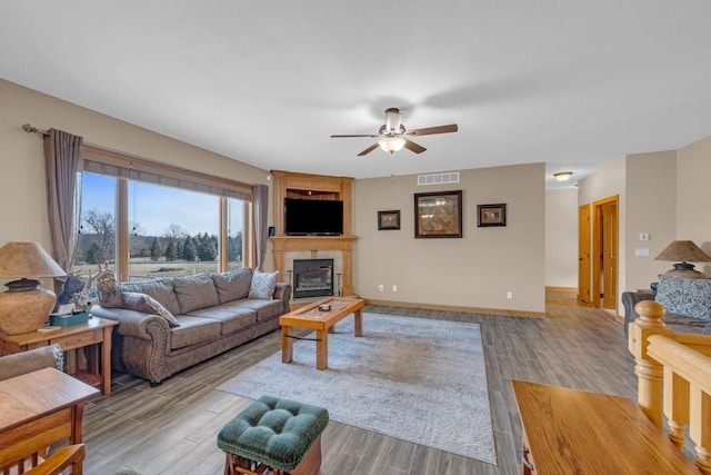 living room with a tiled fireplace, ceiling fan, and light wood-type flooring