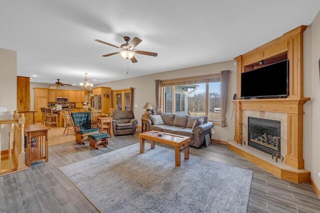 living room with a tiled fireplace, ceiling fan with notable chandelier, and light hardwood / wood-style flooring