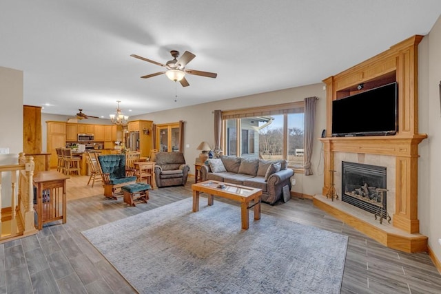 living room featuring ceiling fan with notable chandelier, a fireplace, and light hardwood / wood-style floors