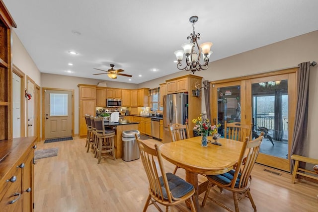 dining room featuring ceiling fan with notable chandelier and light hardwood / wood-style flooring