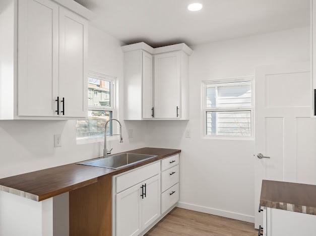 kitchen featuring white cabinetry, sink, wood counters, and light hardwood / wood-style flooring