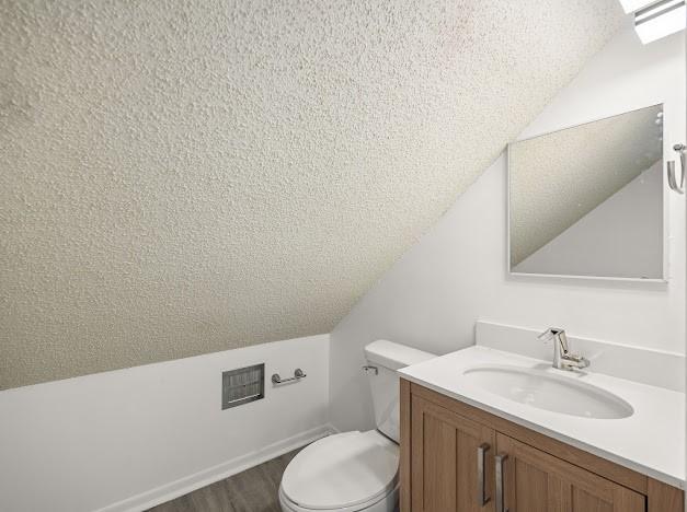 bathroom featuring lofted ceiling, toilet, vanity, and a textured ceiling