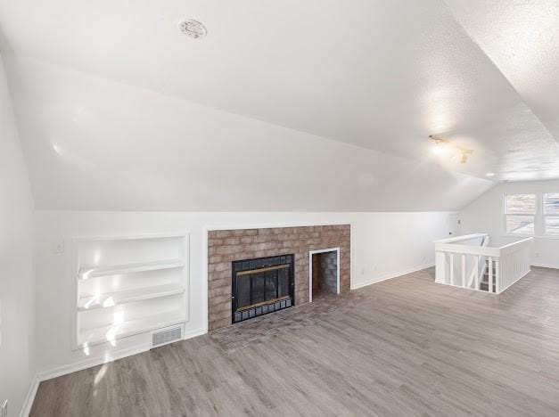 unfurnished living room featuring hardwood / wood-style floors, a fireplace, lofted ceiling, a textured ceiling, and built in shelves