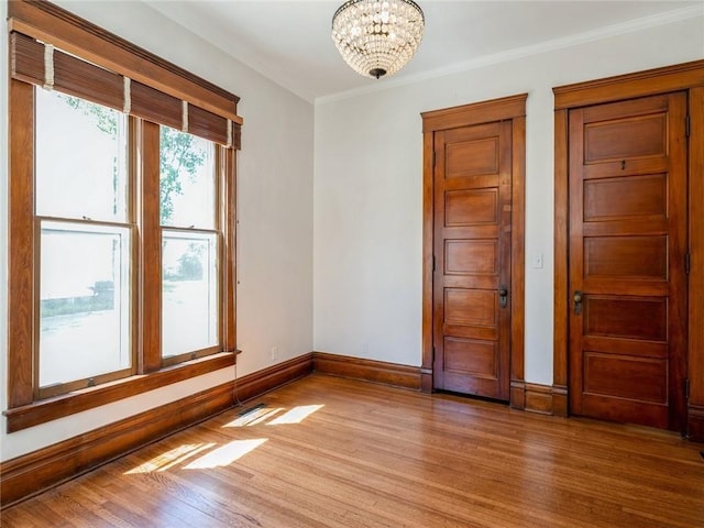 empty room featuring crown molding, hardwood / wood-style floors, and an inviting chandelier