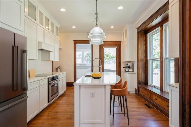 kitchen featuring appliances with stainless steel finishes, white cabinetry, hanging light fixtures, a kitchen island with sink, and plenty of natural light