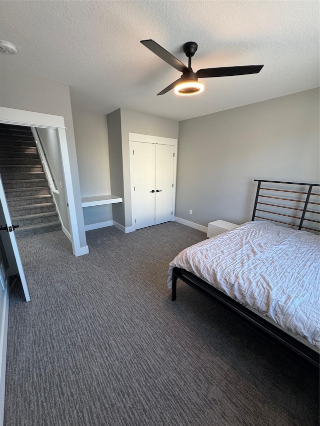 bedroom featuring ceiling fan, a textured ceiling, dark carpet, and a closet