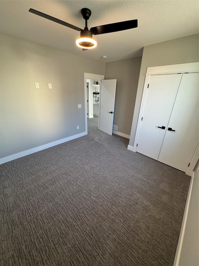 unfurnished bedroom with a closet, ceiling fan, dark carpet, and a textured ceiling