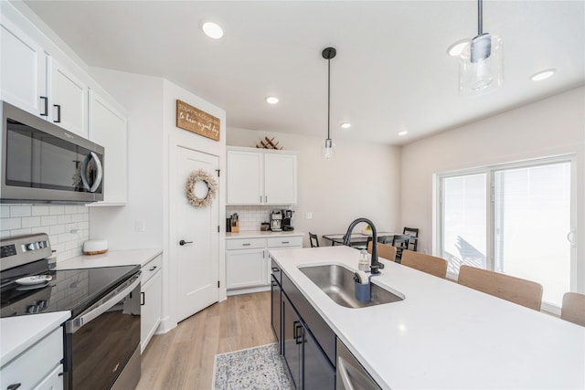 kitchen with sink, white cabinetry, hanging light fixtures, appliances with stainless steel finishes, and light hardwood / wood-style floors