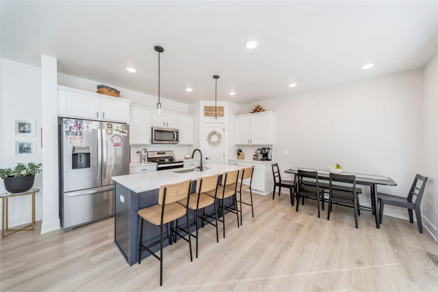 kitchen featuring pendant lighting, sink, white cabinets, stainless steel appliances, and a center island with sink