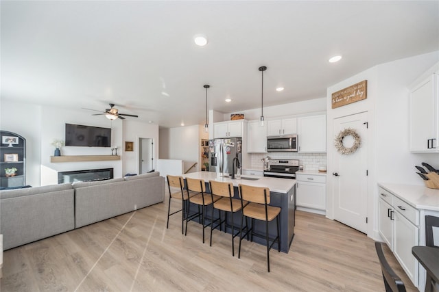 kitchen featuring white cabinetry, stainless steel appliances, decorative light fixtures, and a center island with sink