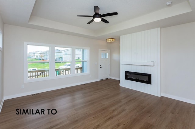 unfurnished living room featuring dark hardwood / wood-style flooring, a tray ceiling, a large fireplace, and ceiling fan