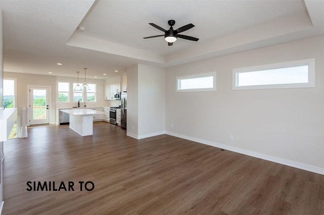 unfurnished living room featuring dark wood-type flooring, sink, ceiling fan, and a tray ceiling