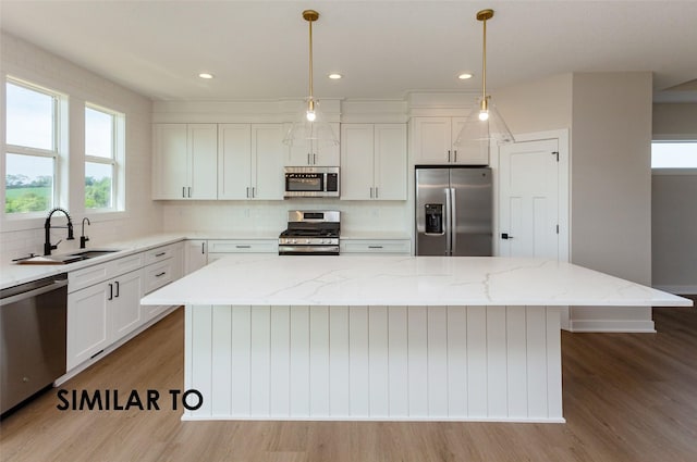 kitchen featuring sink, appliances with stainless steel finishes, light stone countertops, a kitchen island, and decorative light fixtures