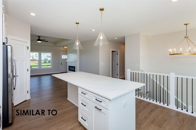 kitchen featuring stainless steel refrigerator, white cabinetry, a center island, light stone counters, and dark hardwood / wood-style flooring