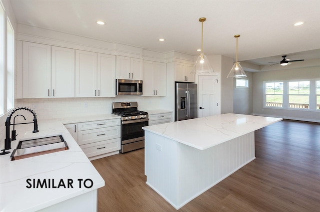 kitchen with sink, white cabinetry, decorative light fixtures, appliances with stainless steel finishes, and a kitchen island