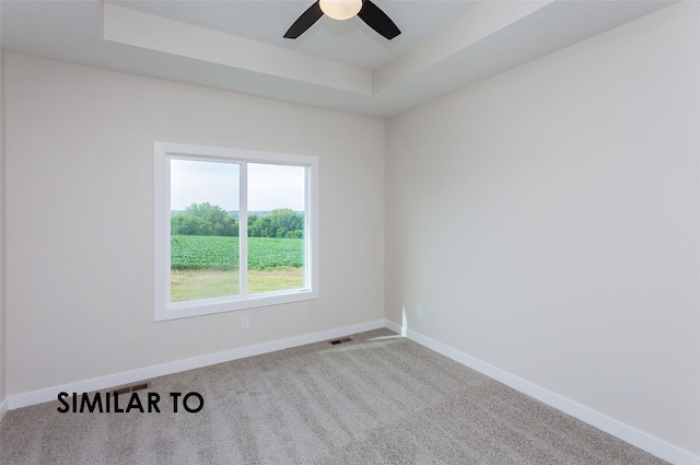 carpeted spare room with a tray ceiling and ceiling fan