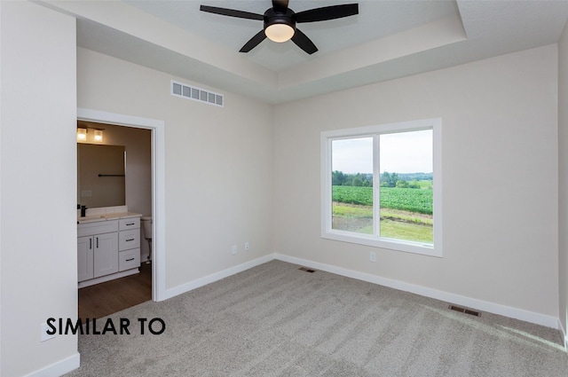 unfurnished bedroom with ensuite bathroom, sink, a raised ceiling, ceiling fan, and carpet