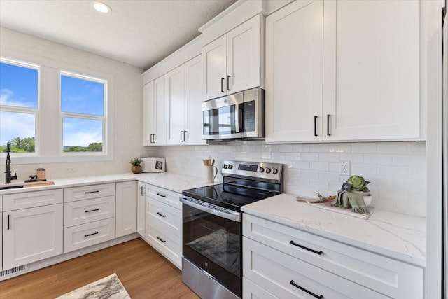 612 W Walnut Pl, Norwalk, IA 50211 - kitchen with appliances with stainless steel finishes, white cabinetry, decorative backsplash, light wood finished floors, and light stone countertops